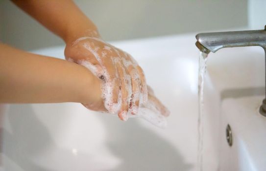 women washing hand with foam soap in bathroom sink.