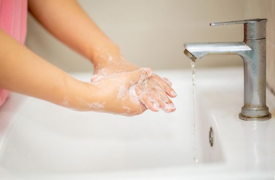 women washing hand with foam soap in bathroom sink.