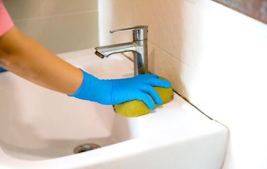 a hand in a blue rubber glove in the picture, removes and washes bathroom sink