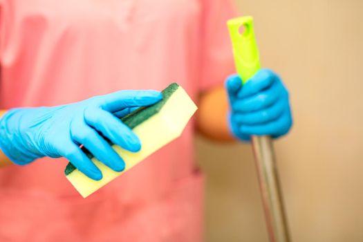 Close-up women hand in a blue rubber glove and cleaning spong in the picture, removes and washes bathroom sink and mirror.