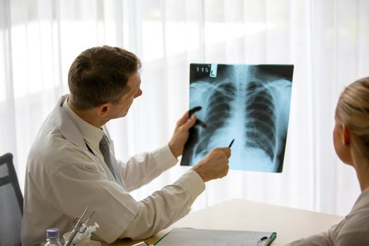 Doctor explaining lungs x-ray to women patient in clinic or Doctor in the office examining an x-ray and discussing with a patient