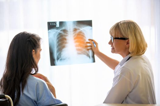 Doctor explaining lungs x-ray to women patient in clinic or Doctor in the office examining an x-ray and discussing with a patient