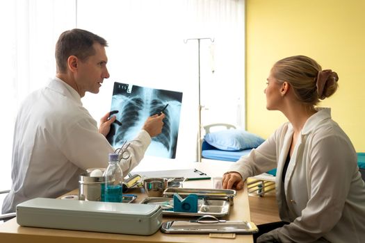 Doctor explaining lungs x-ray to women patient in clinic or Doctor in the office examining an x-ray and discussing with a patient