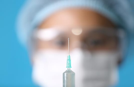 Close-Up Of Syringe Against blurred of doctor face blue Background