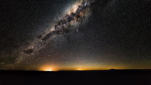 Night landscape with colorful Milky Way and yellow light at mountains. Starry sky with hills at summer. Beautiful Universe. Space background