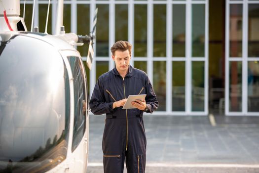 Commercial man pilot in technician suit standing in front of helicopter after check and maintenance engine	