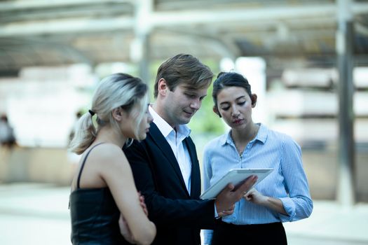 Businessman and women sitting on step outdoor looking on laptop against building