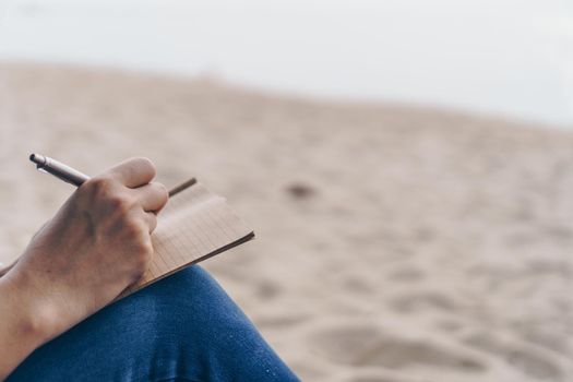 Woman hand writing down in small white memo notebook for take a note not to forget or to do list plan for future.