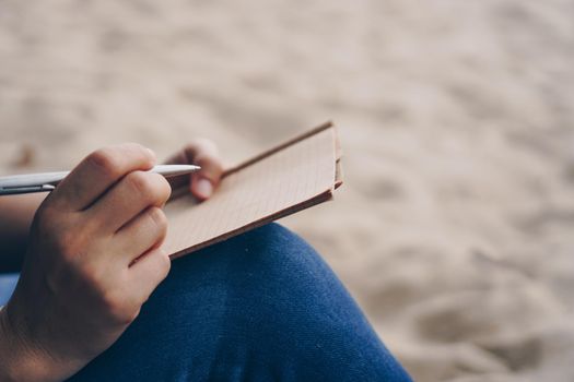 Woman hand writing down in small white memo notebook for take a note not to forget or to do list plan for future.