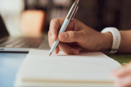 Woman hand writing down in small white memo notebook for take a note not to forget or to do list plan for future.