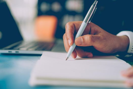 Woman hand writing down in small white memo notebook for take a note not to forget or to do list plan for future.