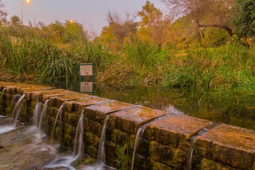 Sunset view of trees, fall foliage, the Kesalon Stream, and a trilingual warning sign, in En Hemed National Park (Aqua Bella), west of Jerusalem, Israel