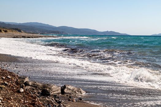Panoramic view at the coastline with pebble beach and water waves on the westside of Greek island Rhodes between Kamiros and Mandriko