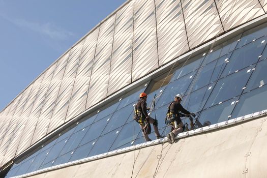 Zaragoza, Spain - Sep. 30, 2020: Specialist technical workers carry out maintenance and rehabilitation work, wearing safety harnesses, on the facade of the Zaragoza bridge pavilion.