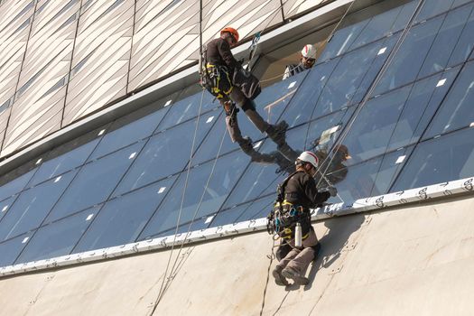 Zaragoza, Spain - Sep. 30, 2020: Specialist technical workers carry out maintenance and rehabilitation work, wearing safety harnesses, on the facade of the Zaragoza bridge pavilion.