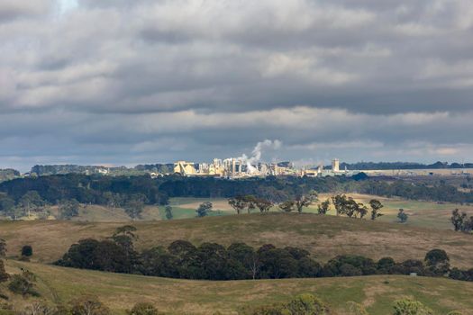 A large manufacturing facility in a regional township with steam coming from the chimney stacks during processing