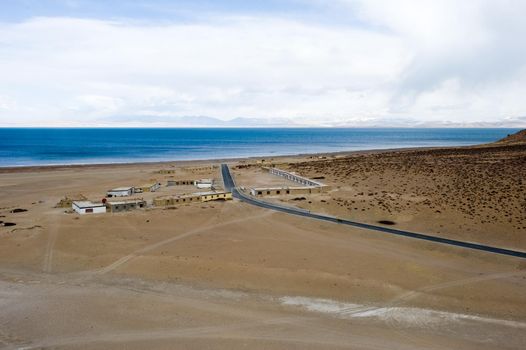 A village near a Tibetan lake and a road to it. A lake in the Himalayas. Tibet, a large lake in the highlands.