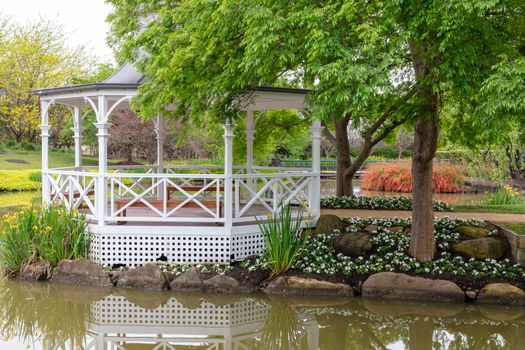 A white pagoda surrounded by trees and flowers on a large garden pond