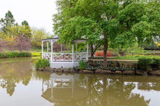 A white pagoda surrounded by trees and flowers on a large garden pond