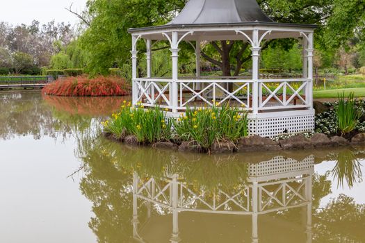 A white pagoda surrounded by trees and flowers on a large garden pond