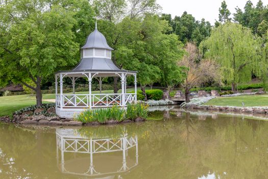 A white pagoda surrounded by trees and flowers on a large garden pond