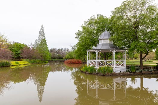 A white pagoda surrounded by trees and flowers on a large garden pond