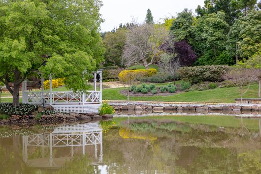 A white pagoda surrounded by trees and flowers on a large garden pond