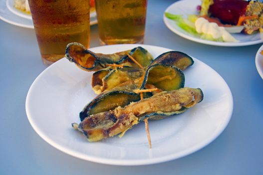 Fried eggplants rolled up with shrimps inside, two beers and other plates