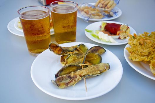 Fried eggplants rolled up with shrimps inside, two beers and other plates