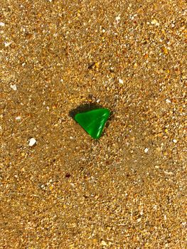 Green triangle glass on the yellow sand, summer, morning