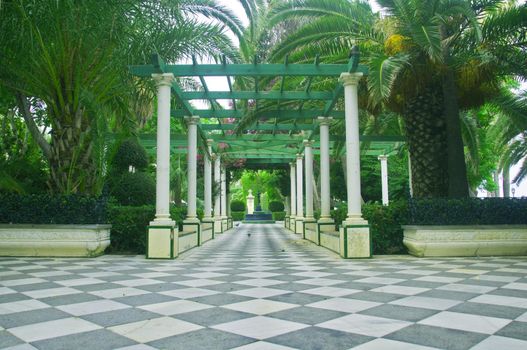 Gallery with white columns and green trees in the park, summer