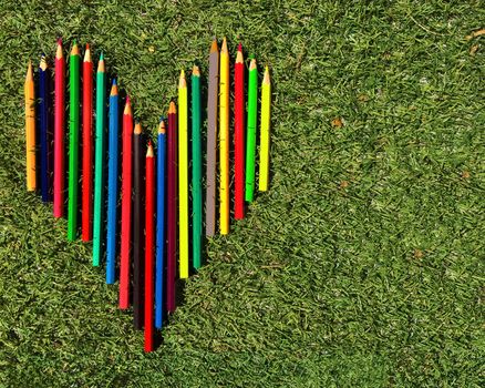 Heart of multicolored pencils on the laying on the grass background.