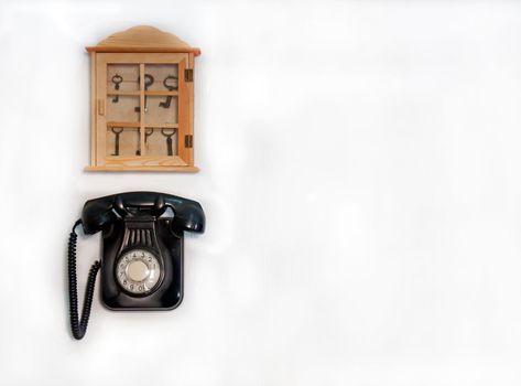 Black old phone and wooden storage with different keys on the white wall