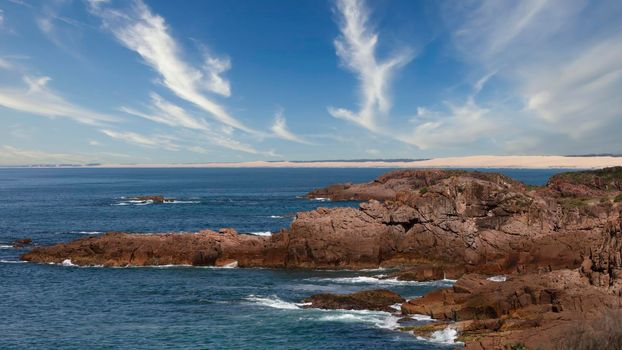 The brown Rocks in front of the Stockton Sand Dunes and blue water of the Tasman Sea at Birubi Point near Port Stephens in regional New South Wales in Australia