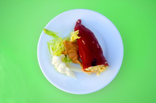 Red stuffed paper with salad and sauce on white plate, isolated