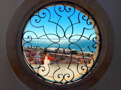 View to the ocean through the round window with figured grid. Lisbon, Portugal