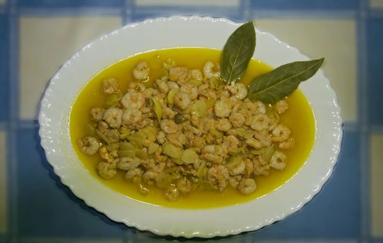 Shrimps in yellow sauce with two bay leaves on white plate