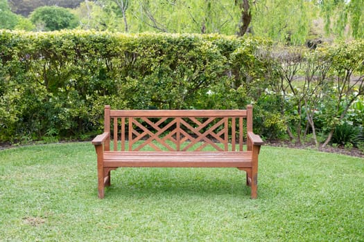 A wooden bench on grass near a hedge in a large garden