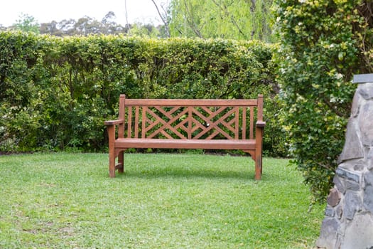 A wooden bench on grass near a hedge in a large garden