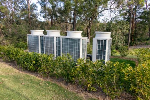 Air conditioner cooling towers outside in a garden surrounded by plants and trees