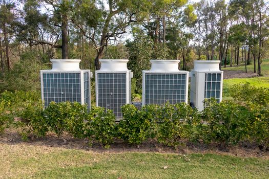 Air conditioner cooling towers outside in a garden surrounded by plants and trees