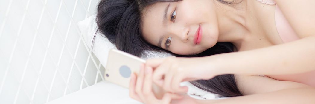 Young asian woman sexy in underwear chatting on mobile phone in the bedroom, happy girl in lingerie looking social media on smartphone lying on bed, communication and lifestyle concept, banner website.