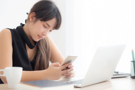 Beautiful young asian woman working laptop computer online to internet and texting message on smart mobile phone, freelance using notebook, business and communication concept.