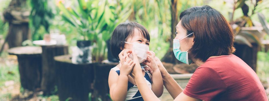 Mother take care daughter with face mask for protection disease flu or covid-19 outdoors, mom wearing on medical mask with child safety for protect pandemic, medical concept, banner website.