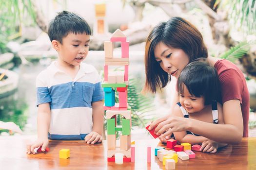 Family with asian mother and children playing toy block at home, mom and son and daughter doing activity and hobby about learning and development, creative and imagination, education concept.