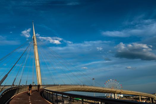 View of the Ponte del Mare, a cycle-pedestrian bridge located in Pescara (Italy). View of the access ramp of the bike path on the north side and the Ferris wheel in the background. Blue sky and clouds in a summer day.