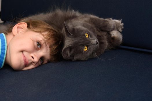 The girl pressed her head to the cat lying on the sofa