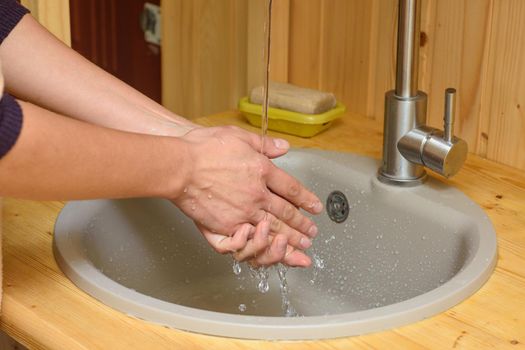 The girl washes her hands under running water in the sink