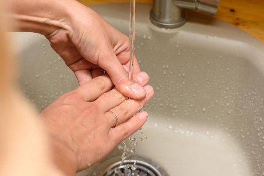 Girl's hands under running water from the tap in the washbasin