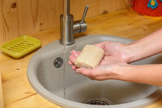 The girl's hands hold soap in the palm, against the background of the washbasin